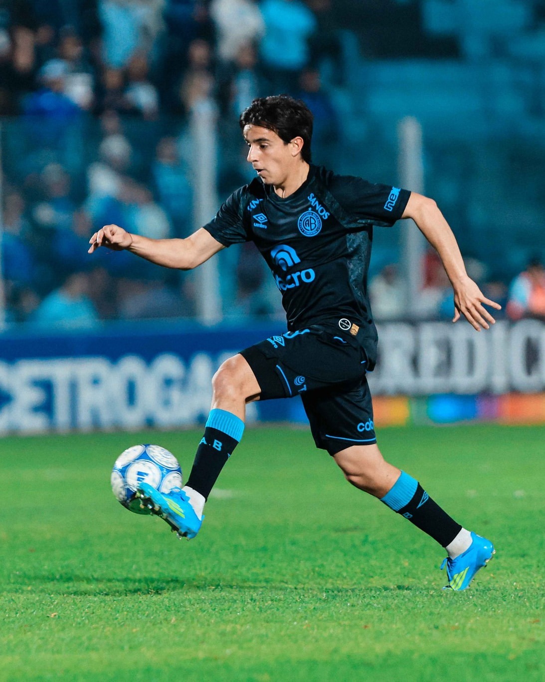 Jugador de Belgrano conduciendo la pelota en un partido nocturno